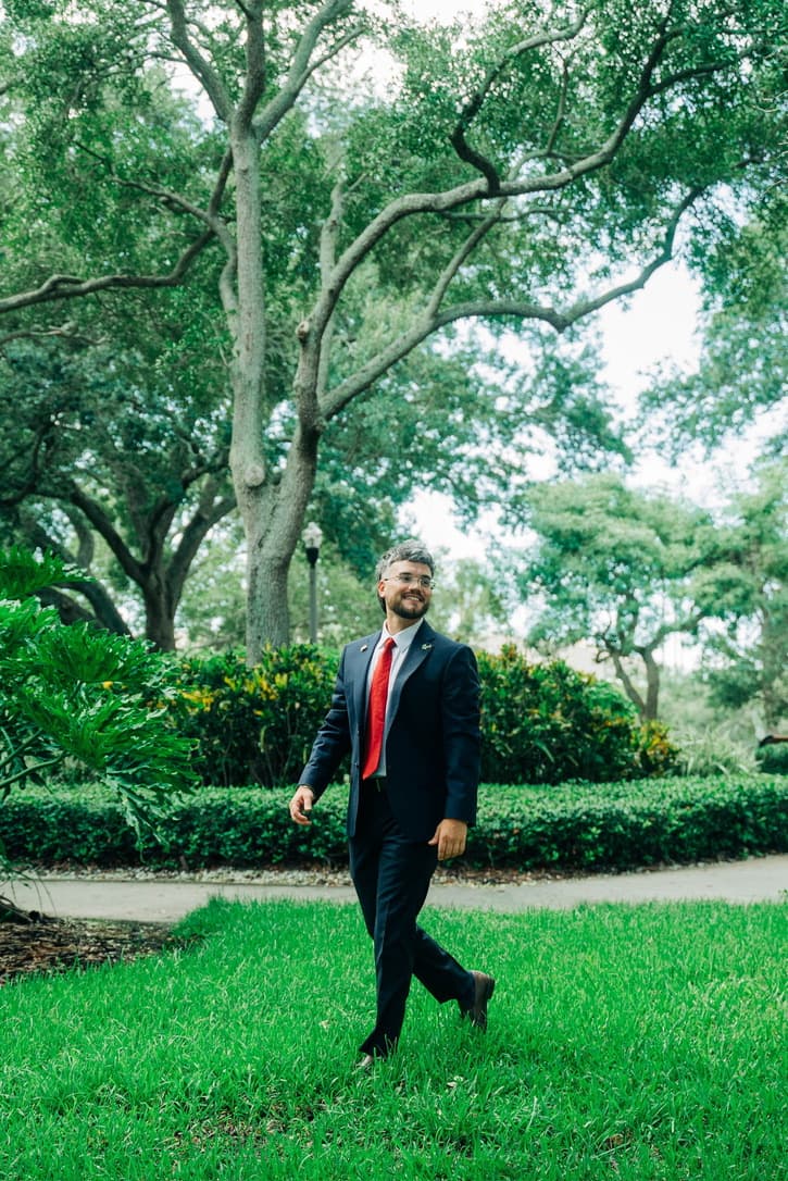 Steven Lombard walking across campus in a navy suit, smiling