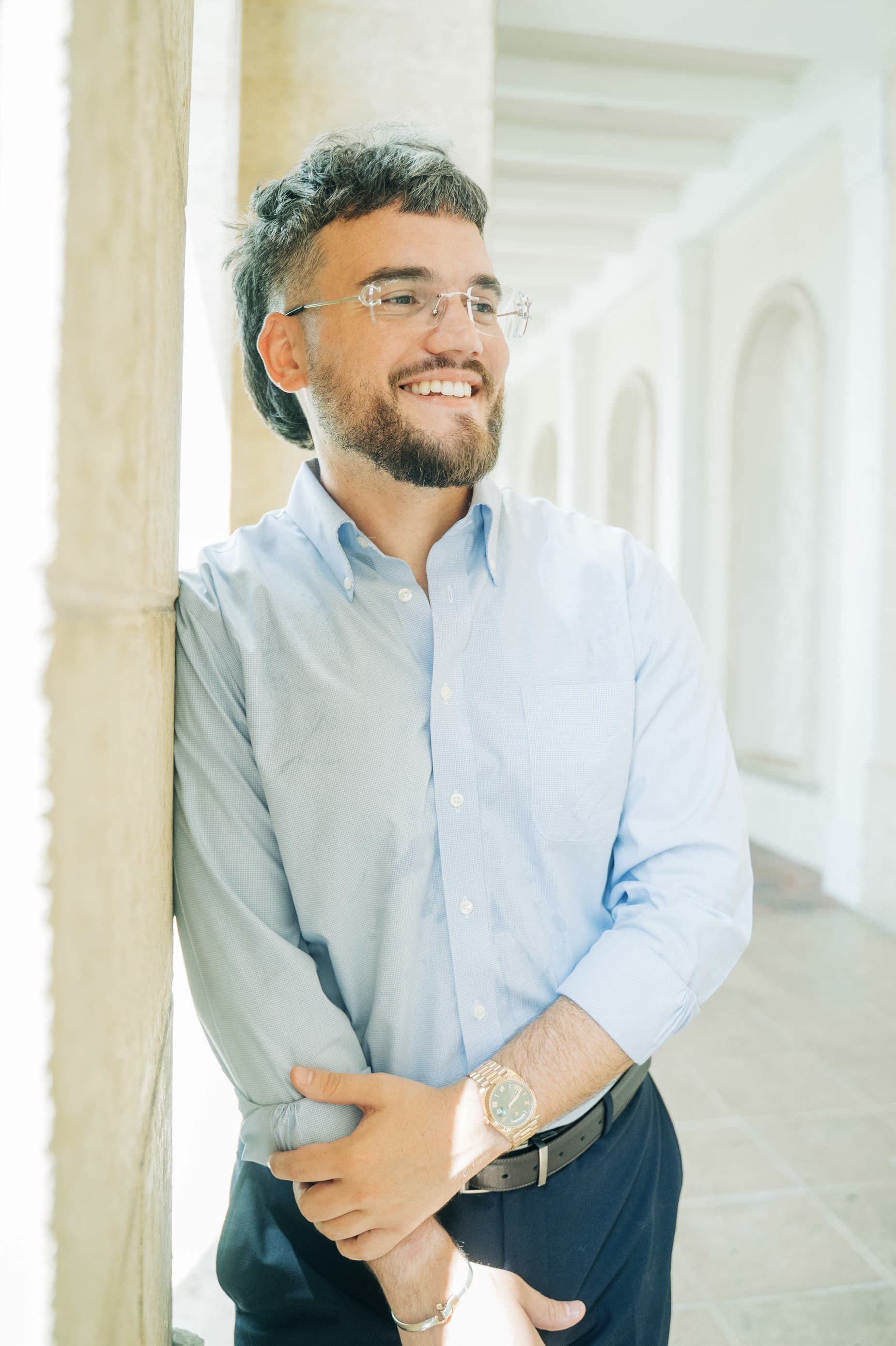 Steven Lombard in a light blue shirt, leaning against a stone column and smiling